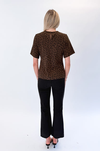 Back view of woman wearing Swagger Boutique’s Leopard Pleated Top with jeans against white studio background.