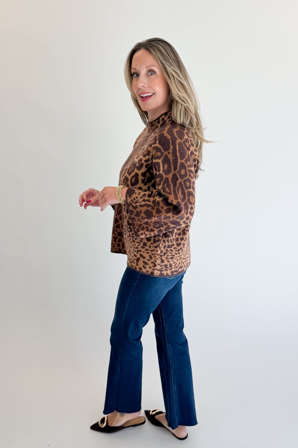 Side view of woman wearing Swagger Boutique’s Leopard Print Mock Neck Sweater by Entro with jeans against white studio background.