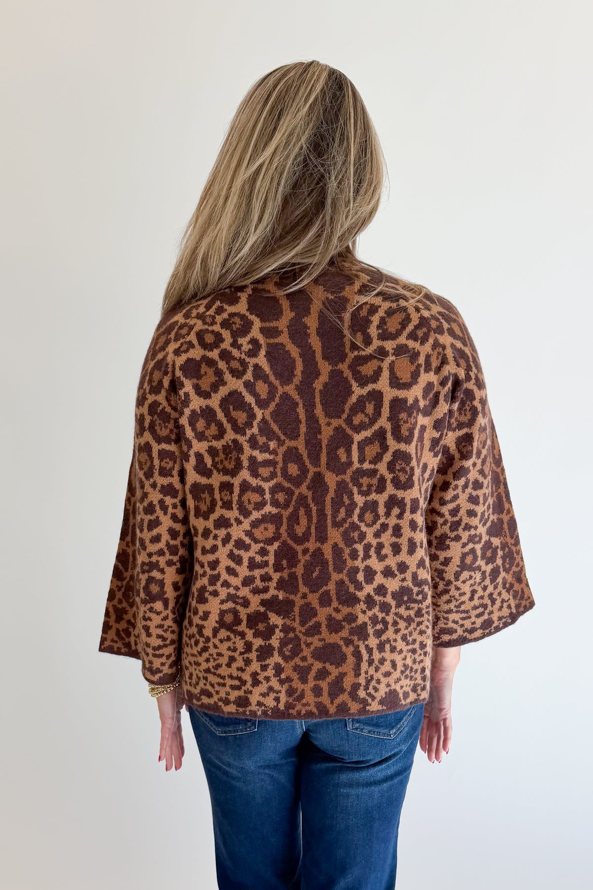 Back view of woman wearing Swagger Boutique’s Leopard Print Mock Neck Sweater by Entro with jeans against white studio background.