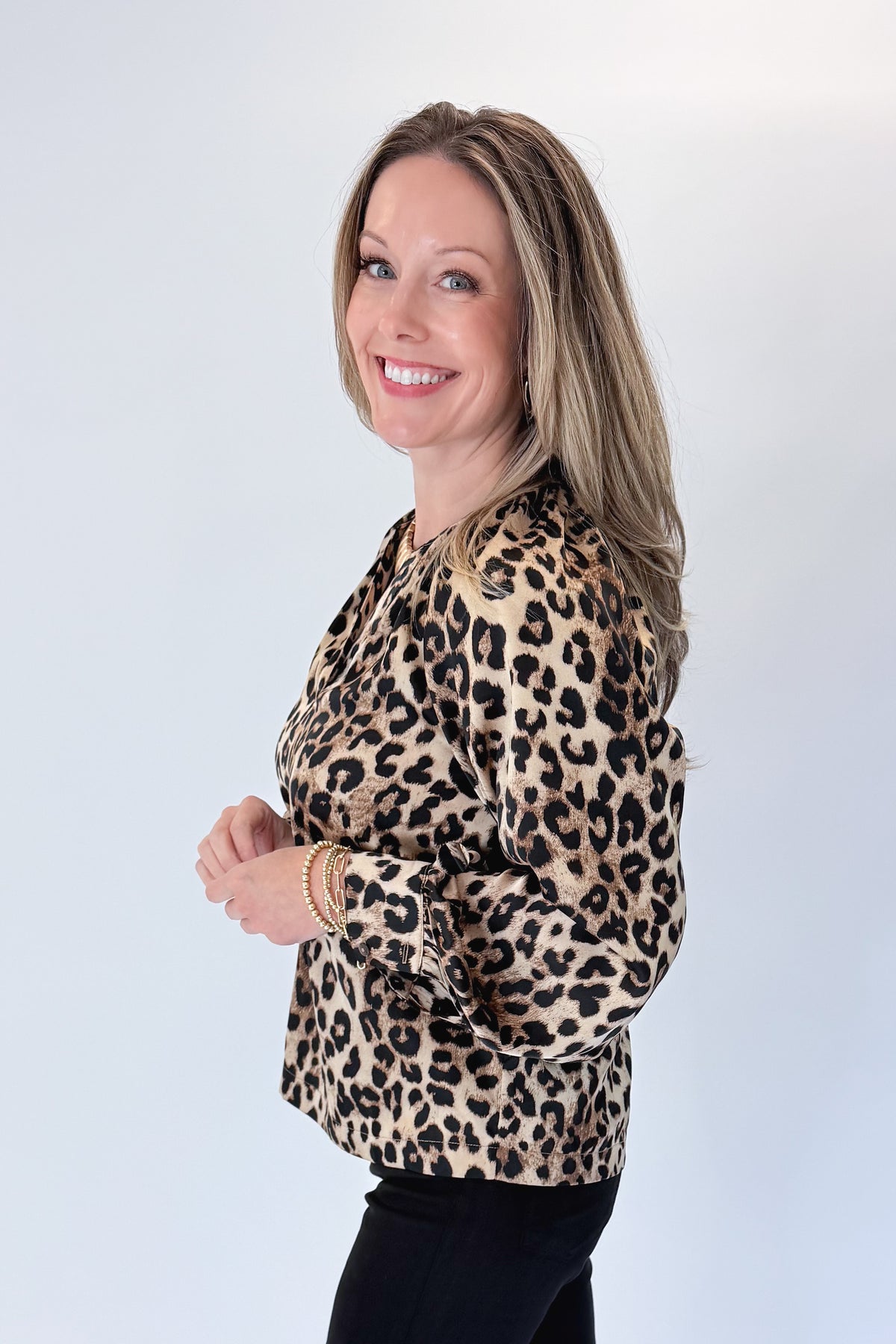 Side view of woman wearing Swagger Boutique’s Leopard Print Silky Top with jeans against white studio background.