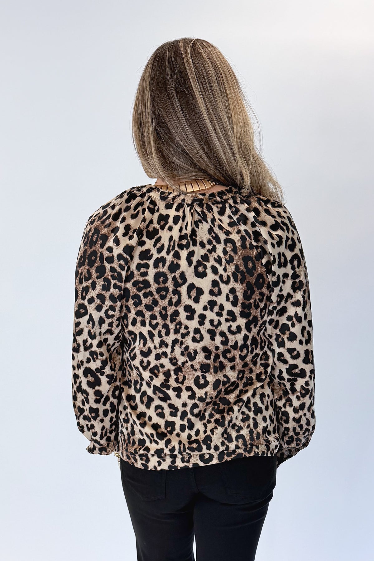 Back view of woman wearing Swagger Boutique’s Leopard Print Silky Top with jeans against white studio background.