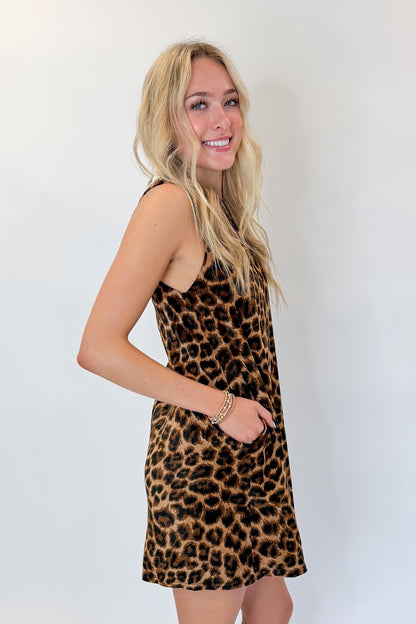 Side view of woman wearing Swagger Boutique’s Leopard Velvet Mini Dress with boots against white studio background.