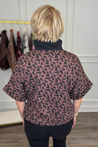Back view of woman wearing Swagger Boutique’s Leopard Half Zip Top by Entro with jeans with clothing hanging in the background.