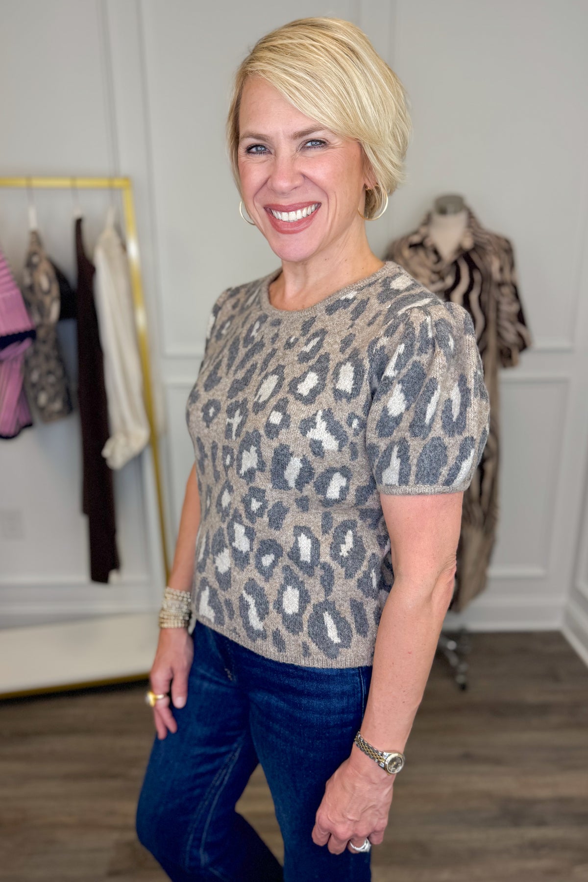 Side view of woman wearing Swagger Boutique’s Leopard Short Sleeve Sweater with jeans with clothing hanging in the background.