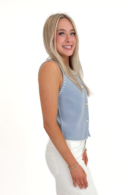 Side view of woman wearing Light Blue Button Up Sleeveless Sweater with white jeans against white studio background.