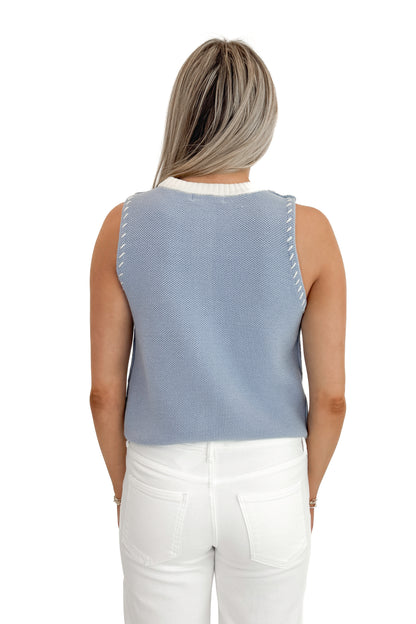 Back view of woman wearing Light Blue Button Up Sleeveless Sweater with white jeans against white studio background.