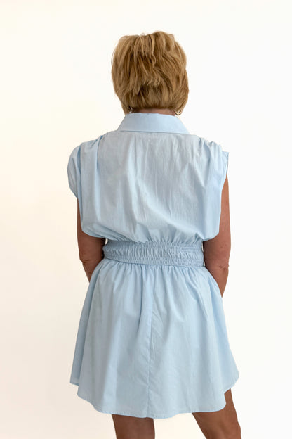 Back view of woman wearing Swagger Boutique’s Light Blue Collared Smocked Waist Dress with sandals against white studio background.
