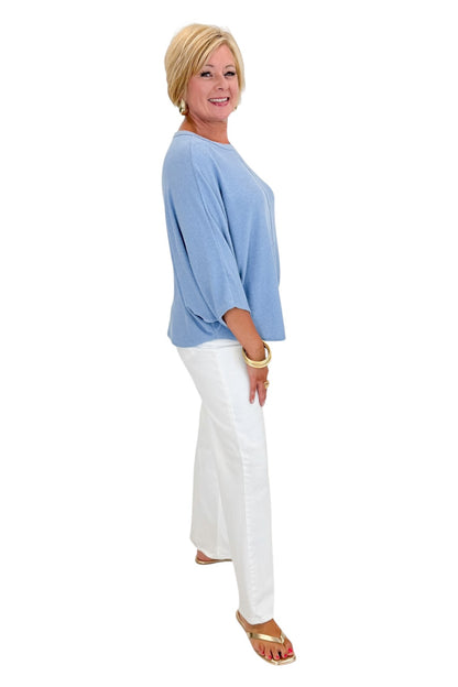 Side view of woman wearing Swagger Boutique’s Light Blue Ribbed Dolman Sleeve Top with jeans against white studio background.