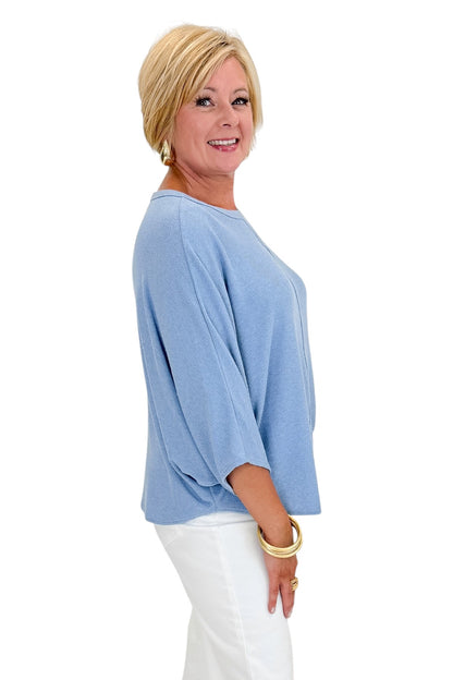 Side view of woman wearing Swagger Boutique’s Light Blue Ribbed Dolman Sleeve Top with jeans against white studio background.