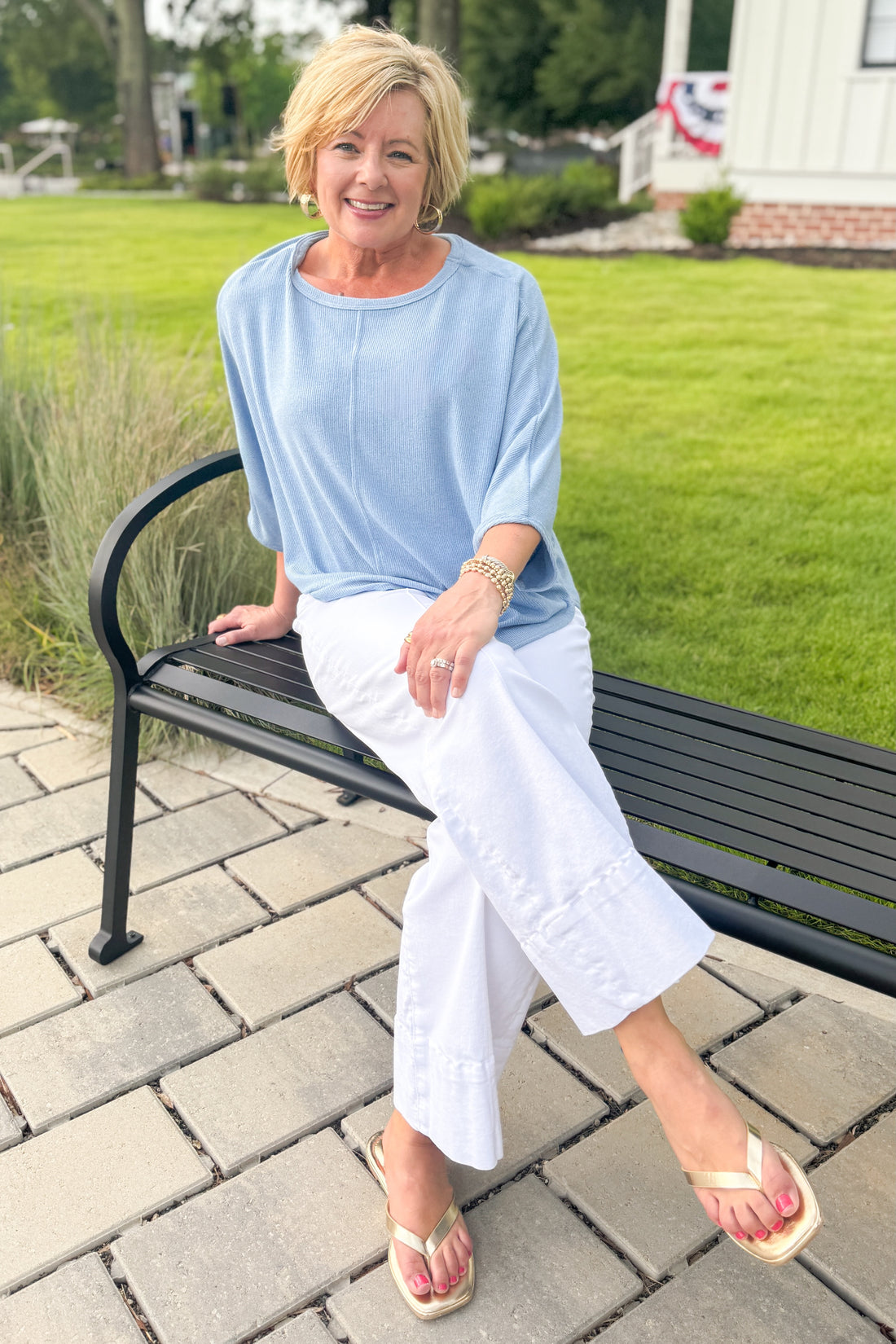 Front view of woman wearing Swagger Boutique’s Light Blue Ribbed Dolman Sleeve Top with jeans sitting outside on a bench.