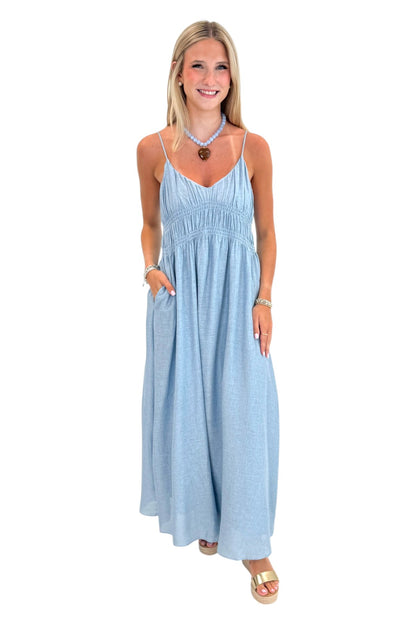 Front view of woman wearing Swagger Boutique’s Light Blue Shirred Linen Maxi Dress with sandals against white studio background.