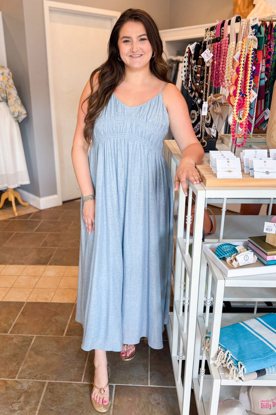 Front view of woman wearing Swagger Boutique’s Light Blue Shirred Linen Maxi Dress with sandals at the store.