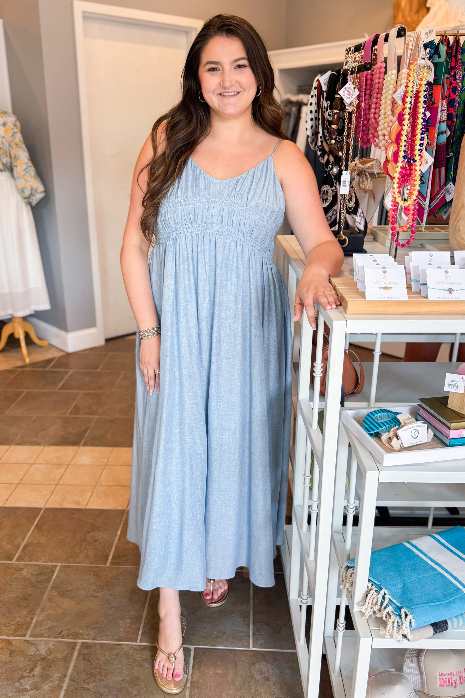 Front view of woman wearing Swagger Boutique’s Light Blue Shirred Linen Maxi Dress with sandals at the store.