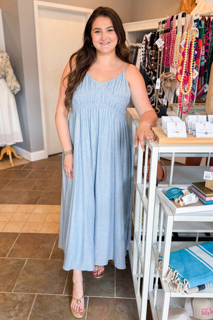 Front view of woman wearing Swagger Boutique’s Light Blue Shirred Linen Maxi Dress with sandals at the store.