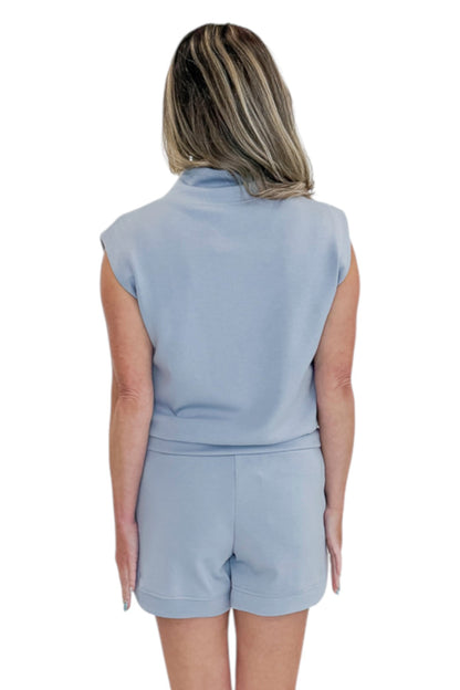 Back view of woman wearing Swagger Boutique’s Light Blue Sleeveless 1/4 Zip Top with matching shorts against white studio background.