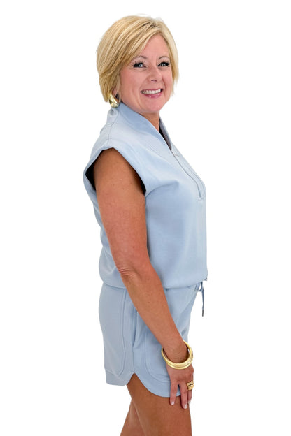 Side view of woman wearing Swagger Boutique’s Light Blue Sleeveless 1/4 Zip Top with matching shorts against white studio background.
