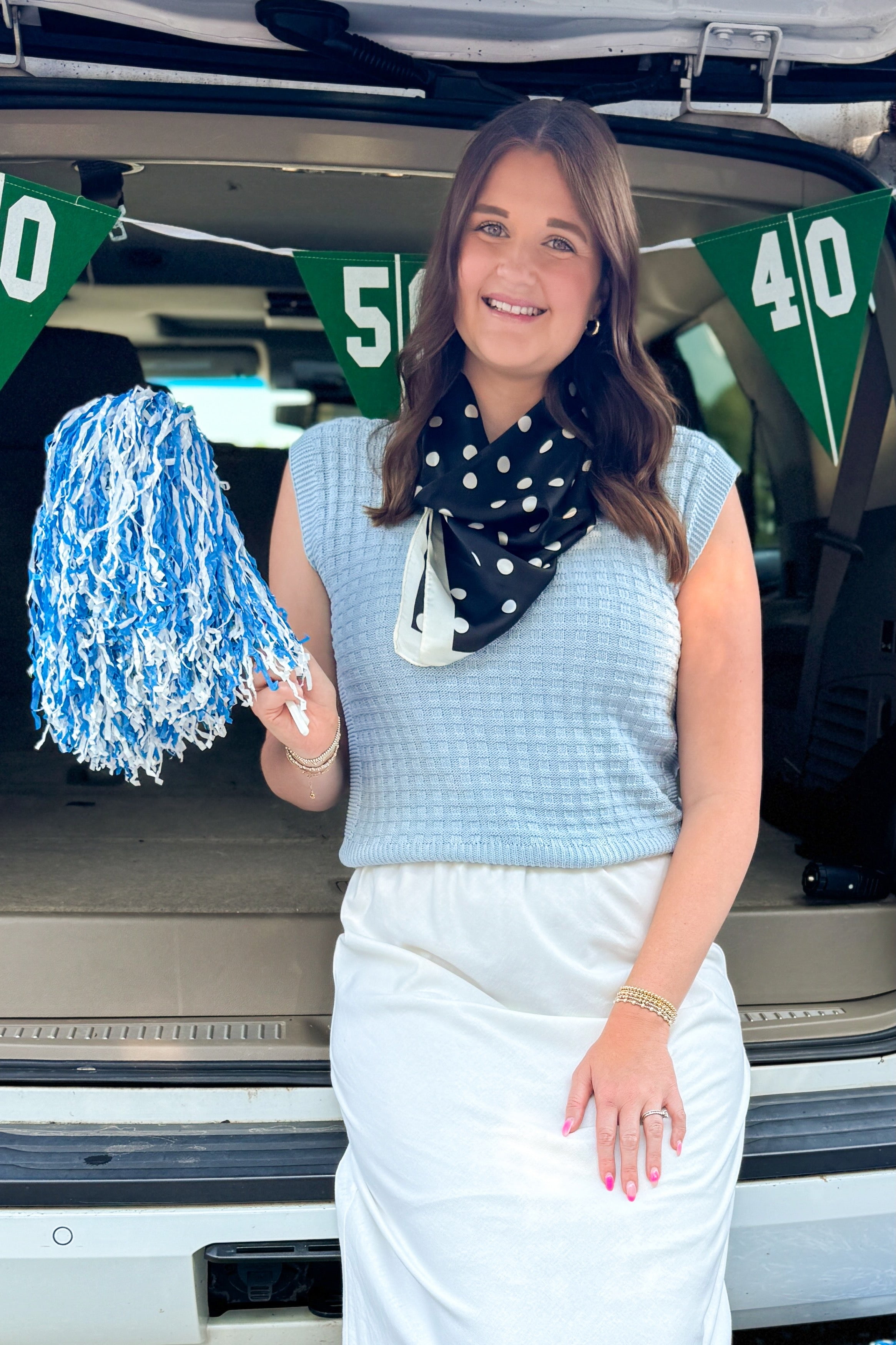 Front view of woman wearing Swagger Boutique’s Light Blue Textured Sleeveless Sweater with skirt at a football tailgate.