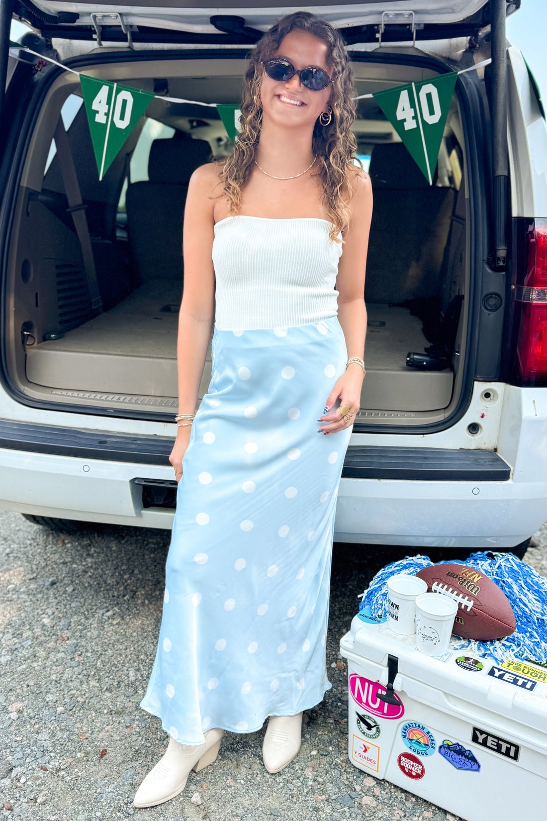 Front view of woman wearing Swagger Boutique’s Light Blue &amp; White Polka Dot Satin Skirt with white top at a football tailgate.