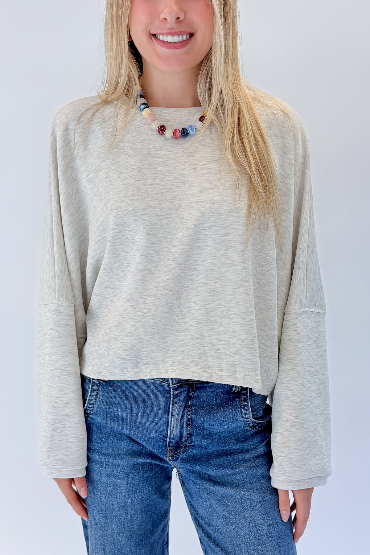 Front detail view of woman wearing Swagger Boutique’s Light Grey Cropped Sweatshirt with jeans against white studio background.