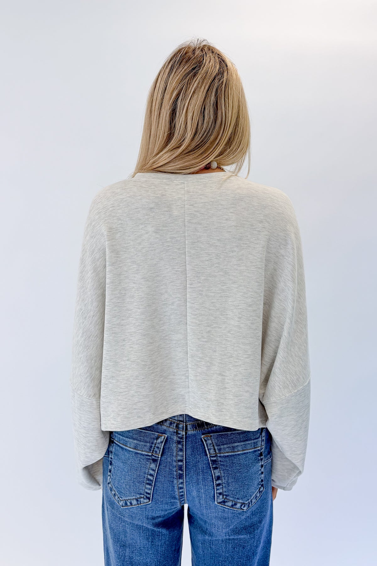 Back view of woman wearing Swagger Boutique’s Light Grey Cropped Sweatshirt with jeans against white studio background.