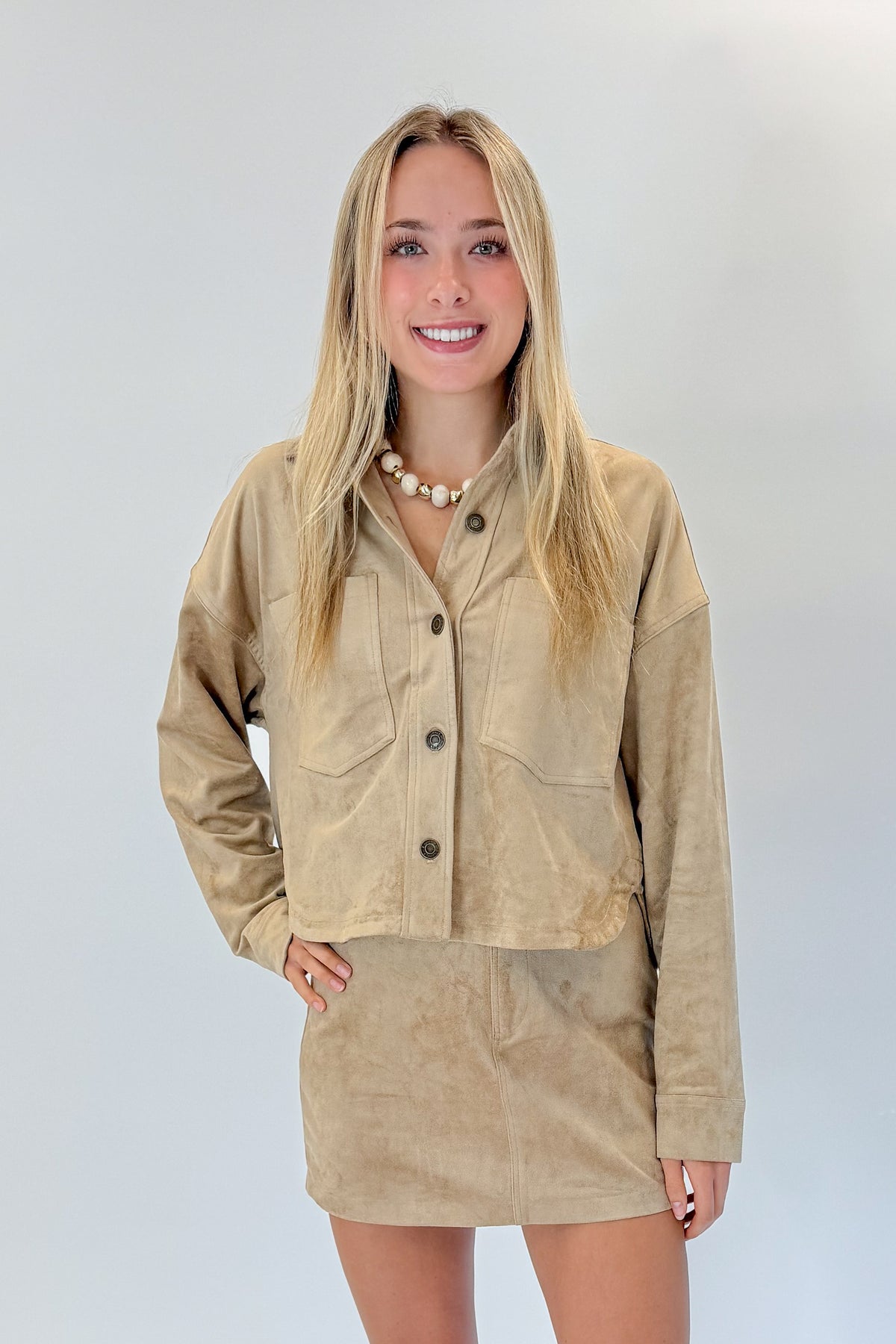 Front view of woman wearing Swagger Boutique’s Light Sand All Day Cropped Suede Jacket and mini skirt by Z Supply against white studio background.