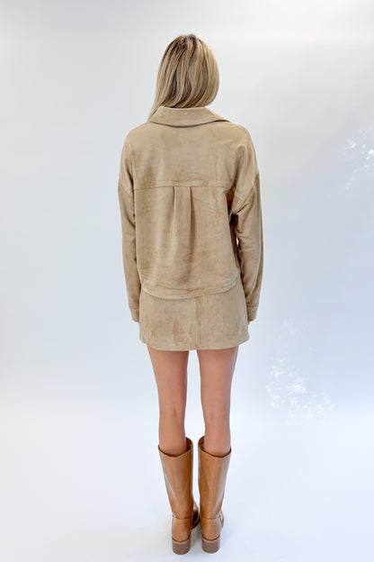 Back view of woman wearing Swagger Boutique’s Light Sand All Day Cropped Suede Jacket and mini skirt by Z Supply against white studio background.