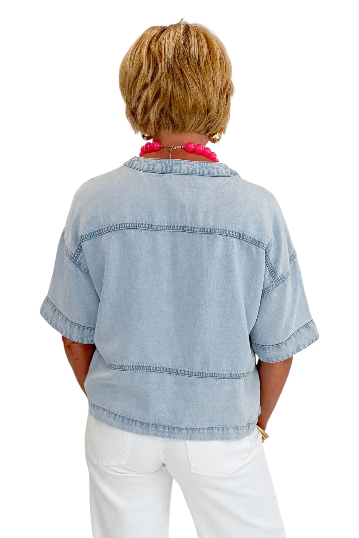 Back view of woman wearing Swagger Boutique’s Light Wash Denim V-Neck Top with jeans against white studio background.