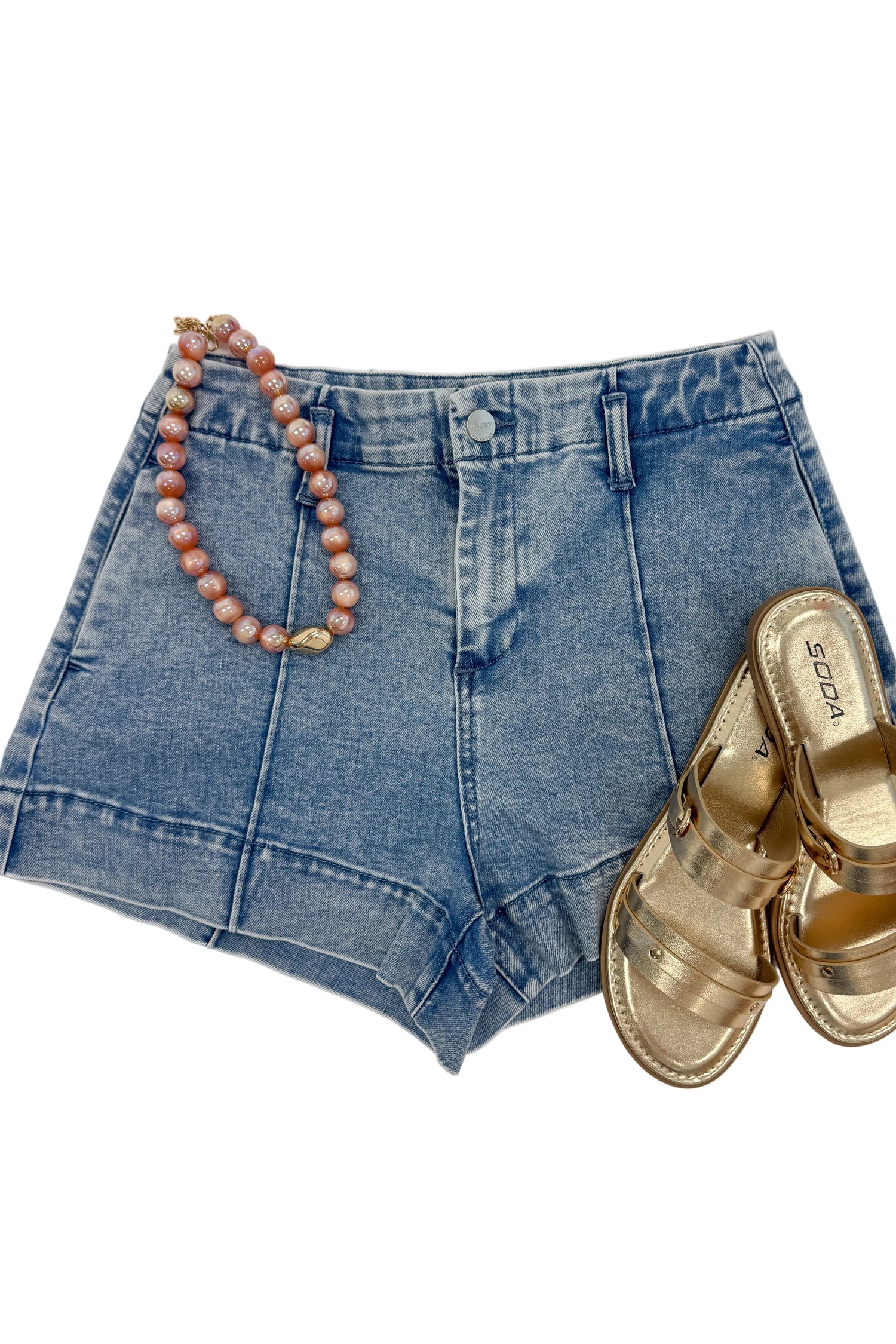 Swagger Boutique’s Light Wash Seamed Denim Shorts with sandals and necklace against white studio background.