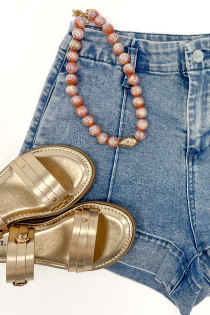 Swagger Boutique’s Light Wash Seamed Denim Shorts with sandals and necklace against white studio background.