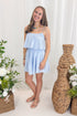 Front view of woman wearing Swagger Boutique’s Light Blue Pleated Mini Dress  and sandals with a decorative background.