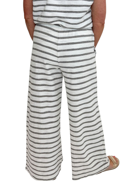 Back detail view of woman wearing Swagger Boutique’s Light Grey Striped Short Sleeve Top with matching Light Grey Striped Lounge Pants against white studio background.