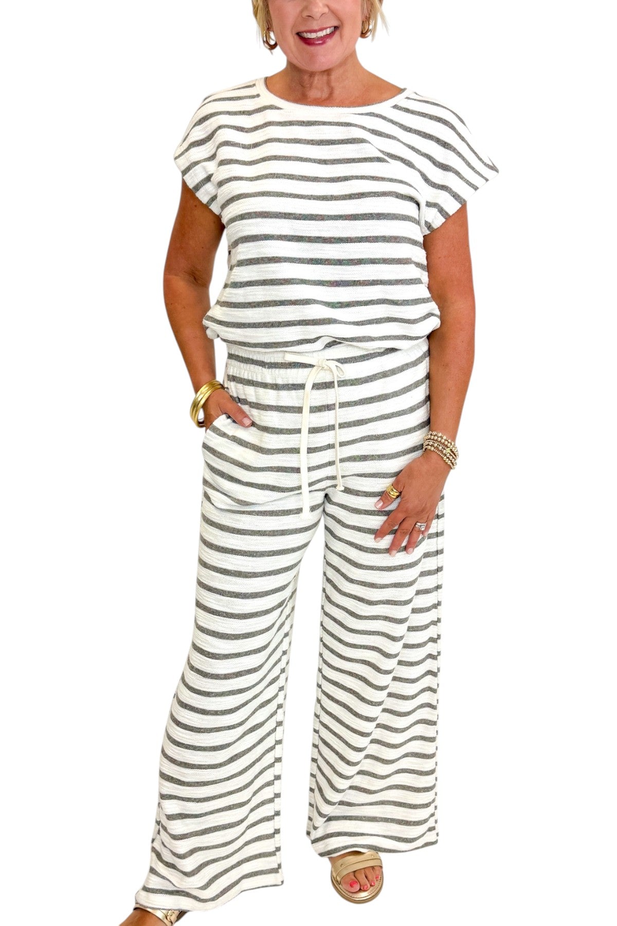 Front detail view of woman wearing Swagger Boutique’s Light Grey Striped Short Sleeve Top with matching Light Grey Striped Lounge Pants against white studio background.