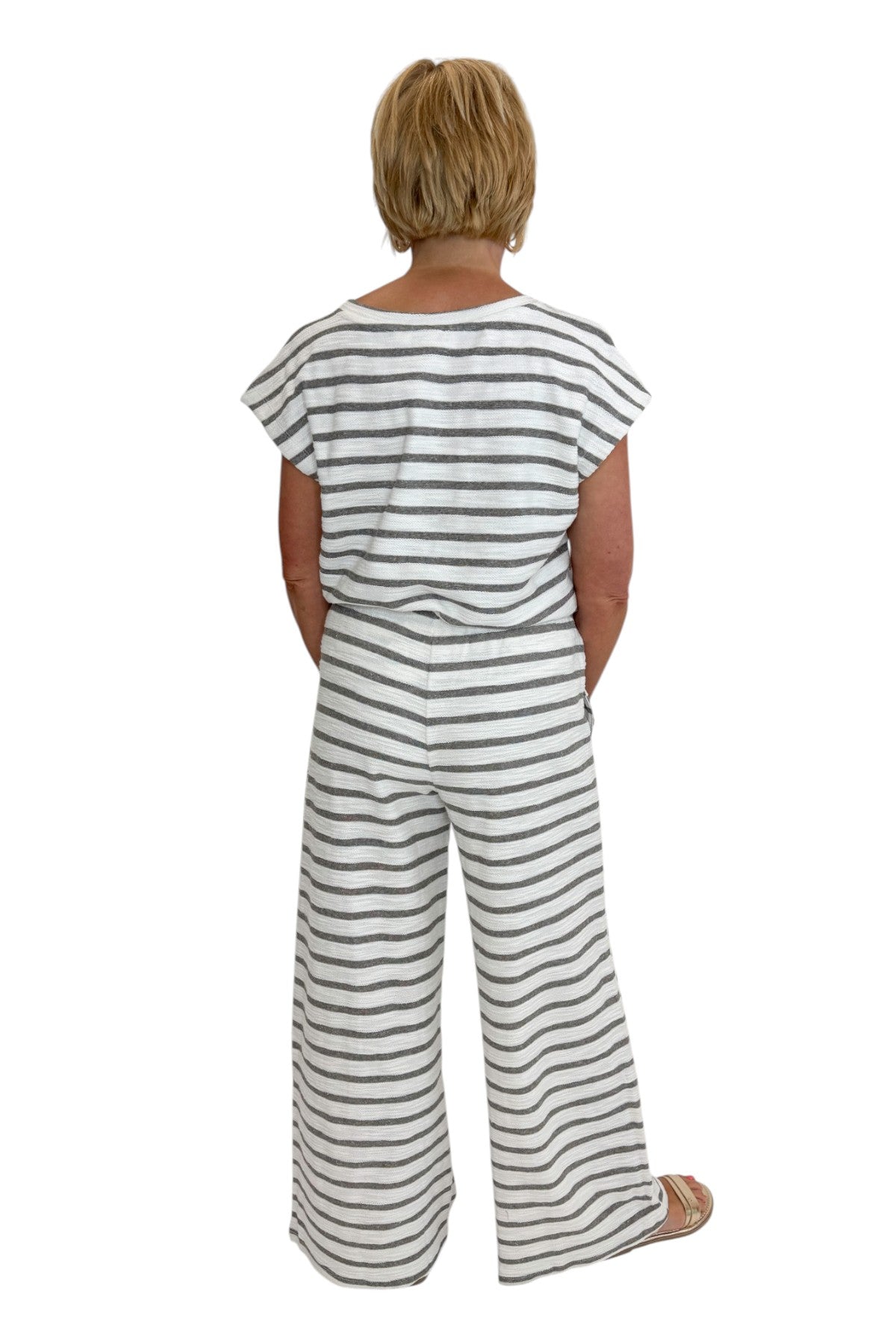 Back view of woman wearing Swagger Boutique’s Light Grey Striped Short Sleeve Top with matching Light Grey Striped Lounge Pants against white studio background.