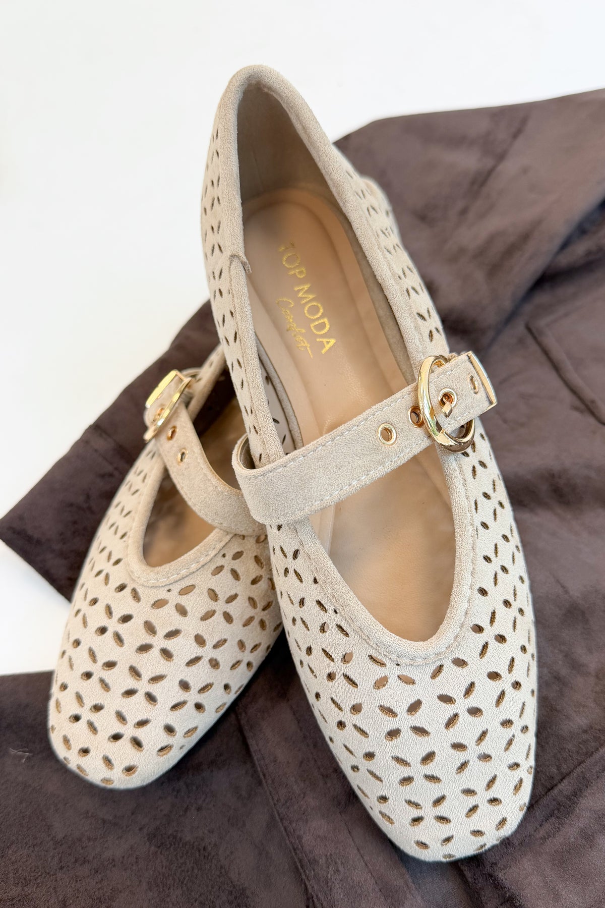 Linda- Sand Suede Flats against white and brown studio background. 