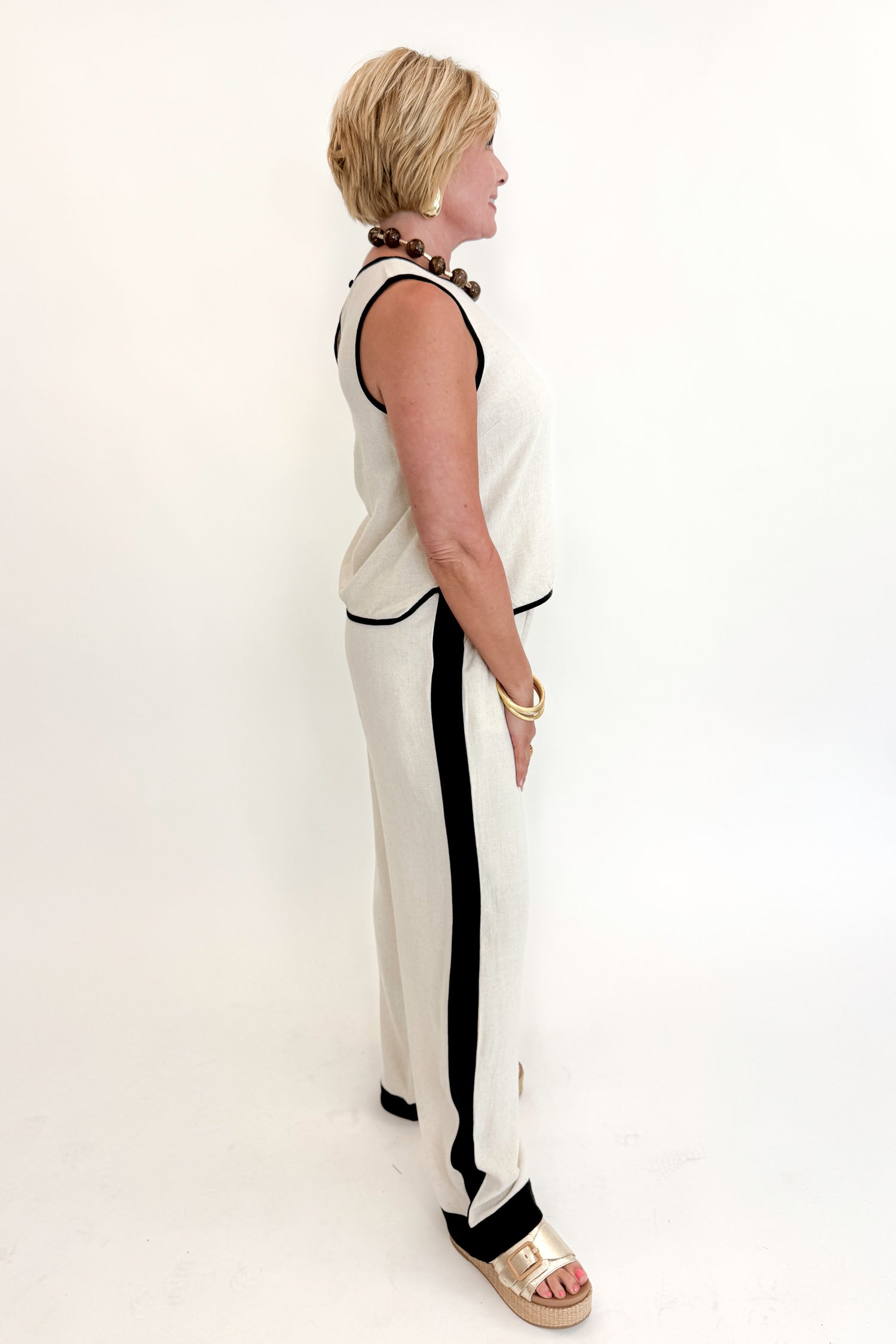 Side view of woman wearing Swagger Boutique’s Linen &amp; Black Lined Tank with matching Linen &amp; Black Stripe Pants against white studio background.