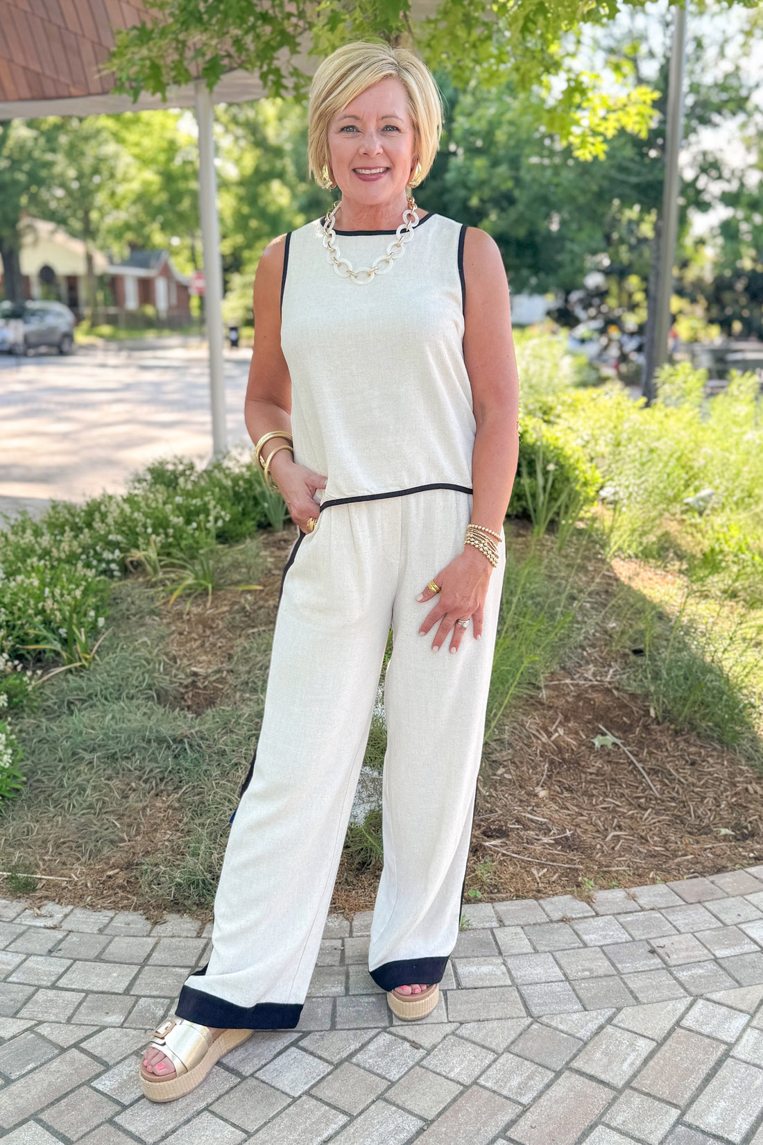 Front view of woman wearing Swagger Boutique’s Linen &amp; Black Lined Tank with matching Linen &amp; Black Stripe Pants and platform sandals outside at a park.