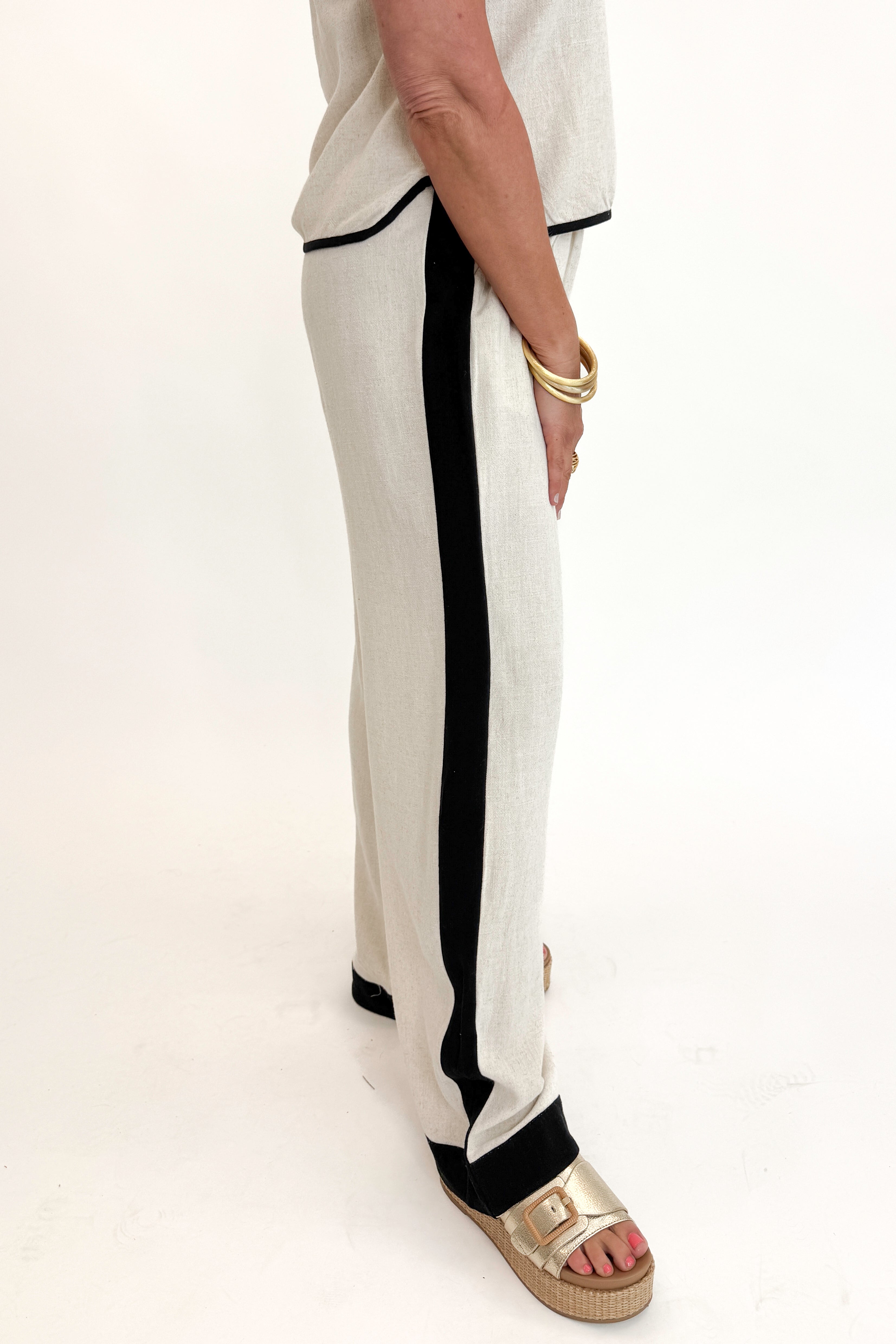 Side detail view of woman wearing Swagger Boutique’s Linen &amp; Black Lined Tank with matching Linen &amp; Black Stripe Pants against white studio background.