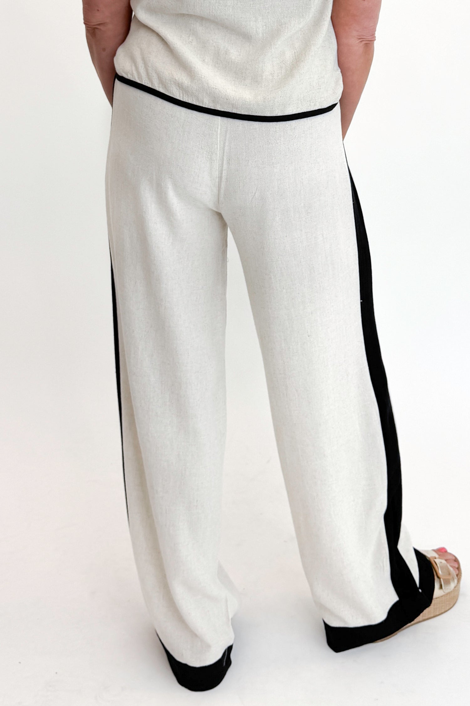 Back detail view of woman wearing Swagger Boutique’s Linen &amp; Black Lined Tank with matching Linen &amp; Black Stripe Pants against white studio background.