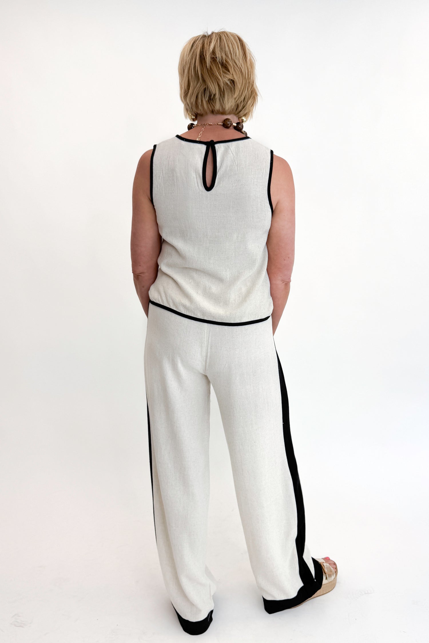 Back view of woman wearing Swagger Boutique’s Linen &amp; Black Lined Tank with matching Linen &amp; Black Stripe Pants against white studio background.