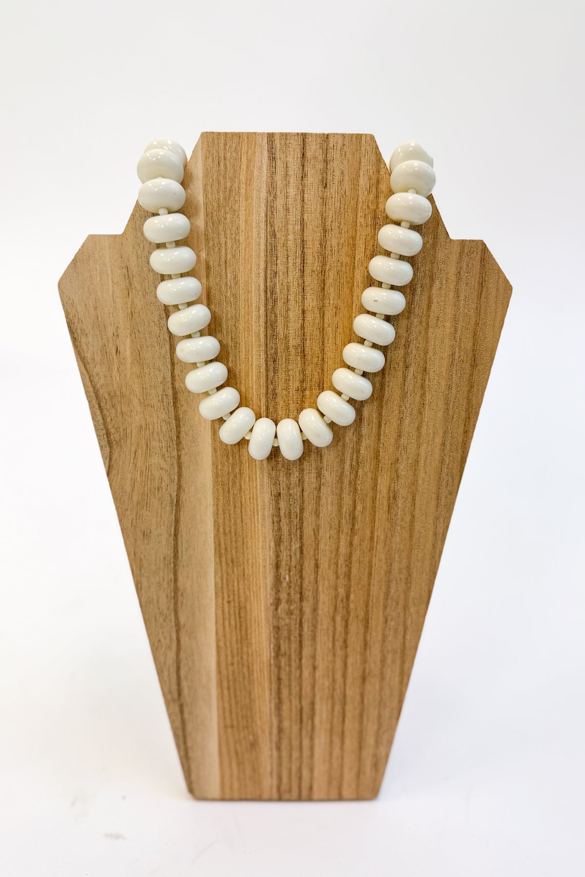 A strand of white, oval-shaped beads draped over a light brown wooden display stand against a plain white background.