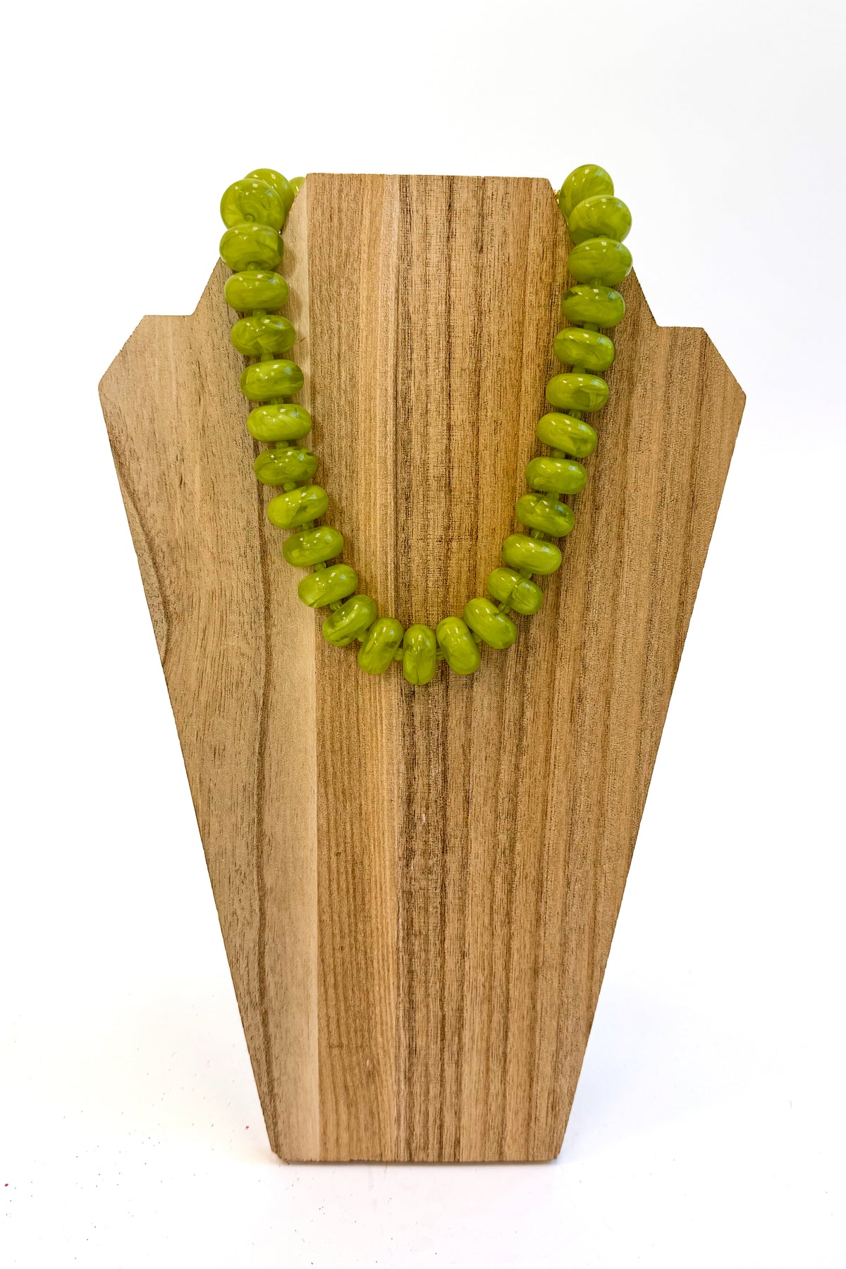 A green beaded necklace displayed on a light wood stand against a white background.