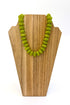 A green beaded necklace displayed on a light wood stand against a white background.