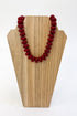 A red beaded necklace displayed on a light wood jewelry bust against a white background.