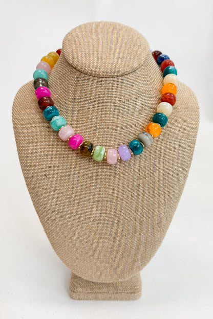 Colorful beaded necklace on a beige jewelry display bust against a white background