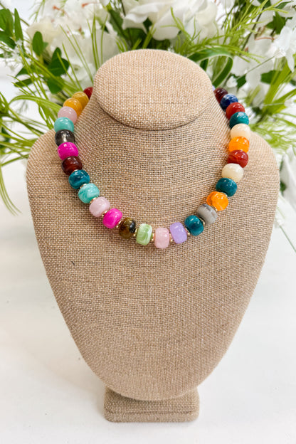 Colorful beaded necklace on a beige jewelry display with greenery in the background