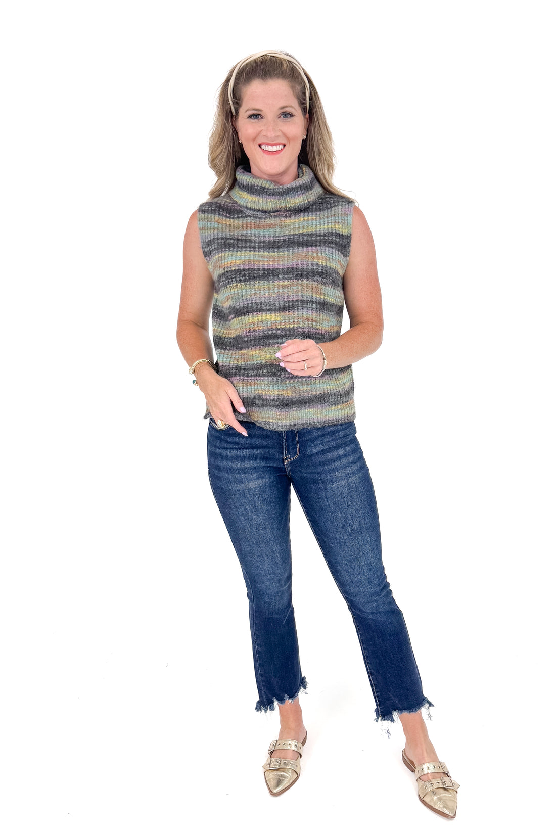 Woman wearing a sleeveless striped sweater and blue jeans on a white background
