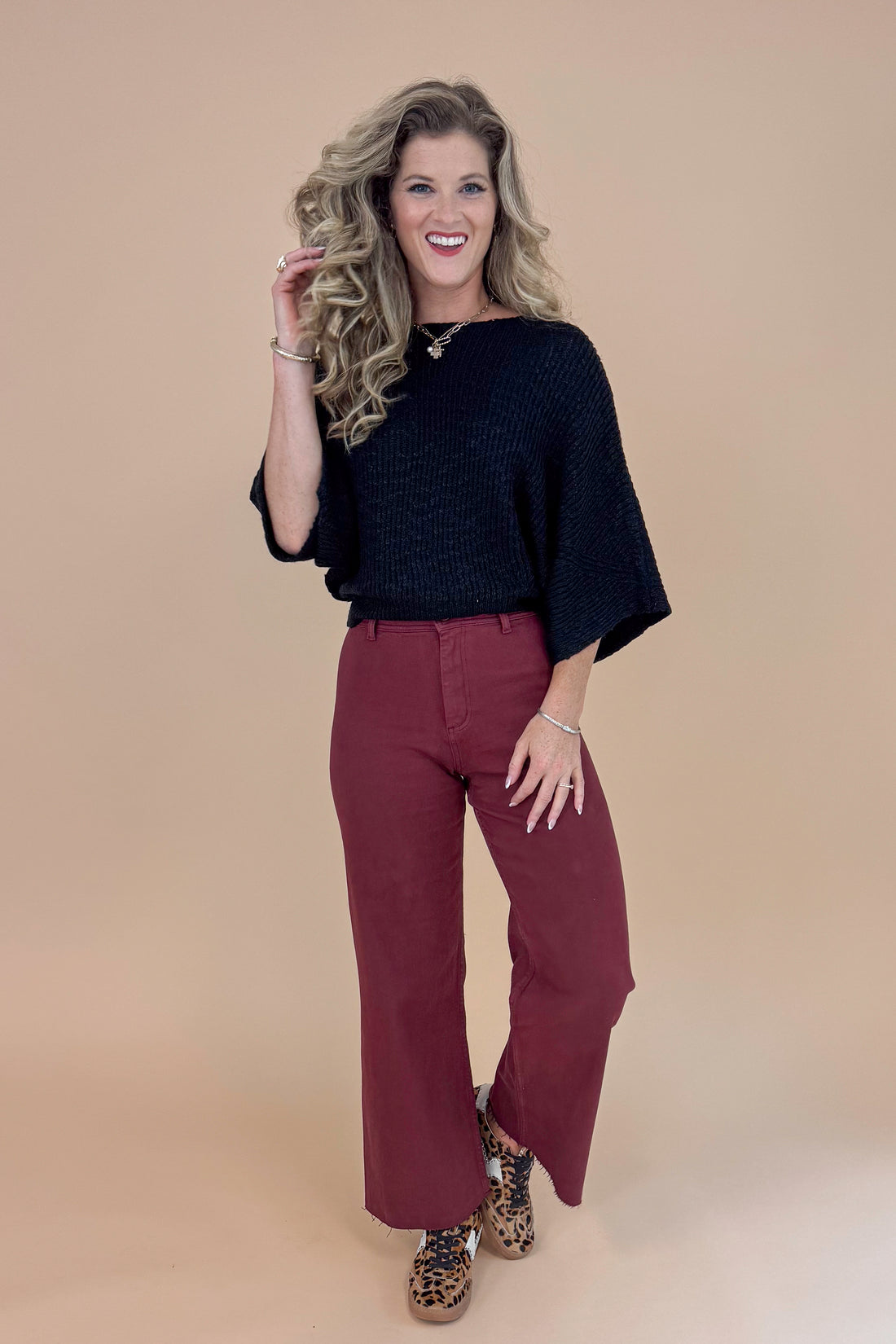 Woman wearing a black top and maroon pants against a beige background