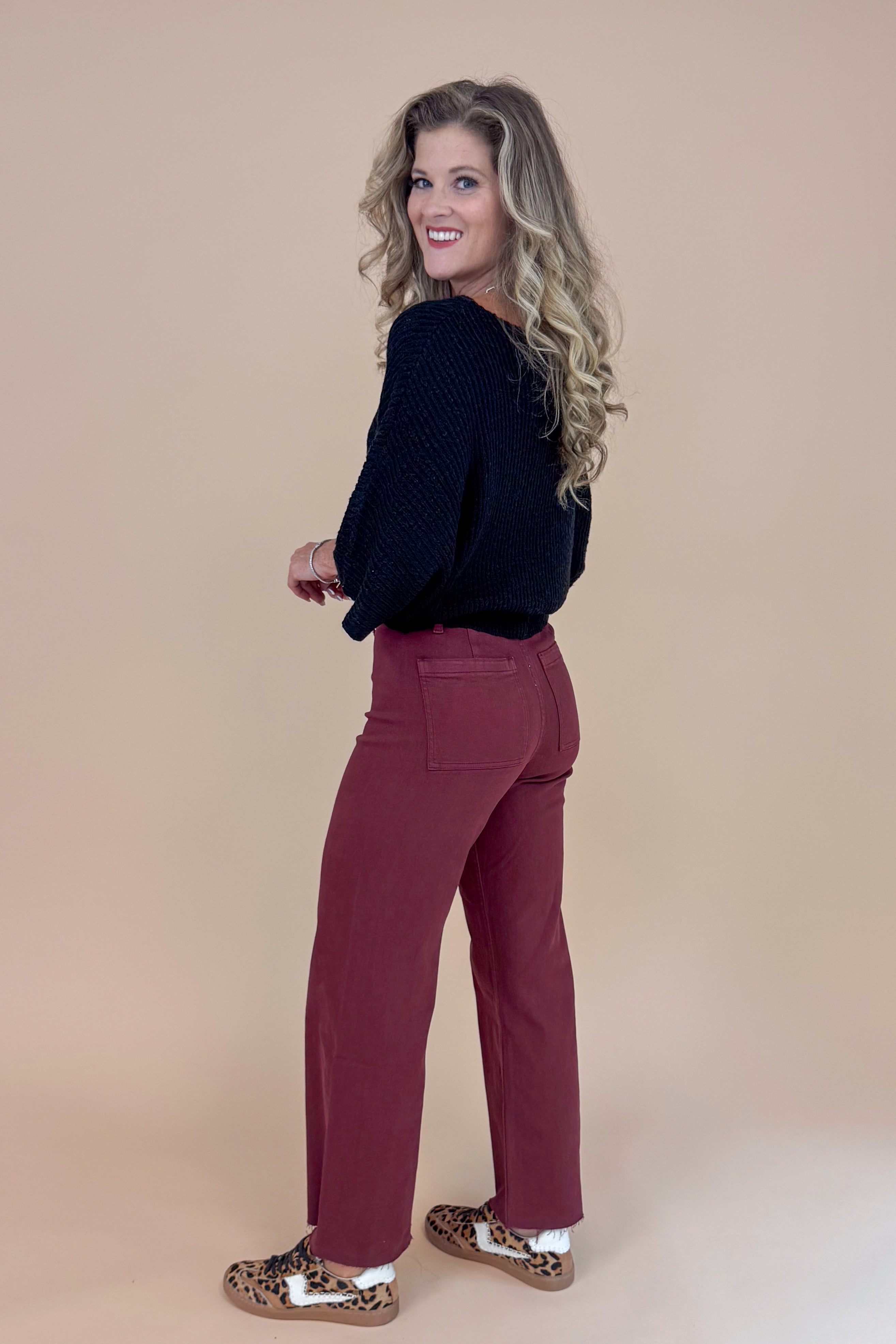 Woman wearing a black top and maroon pants against a beige background