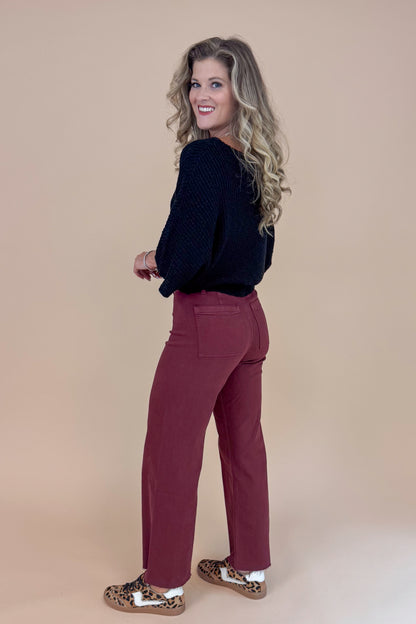 Woman wearing a black top and maroon pants against a beige background