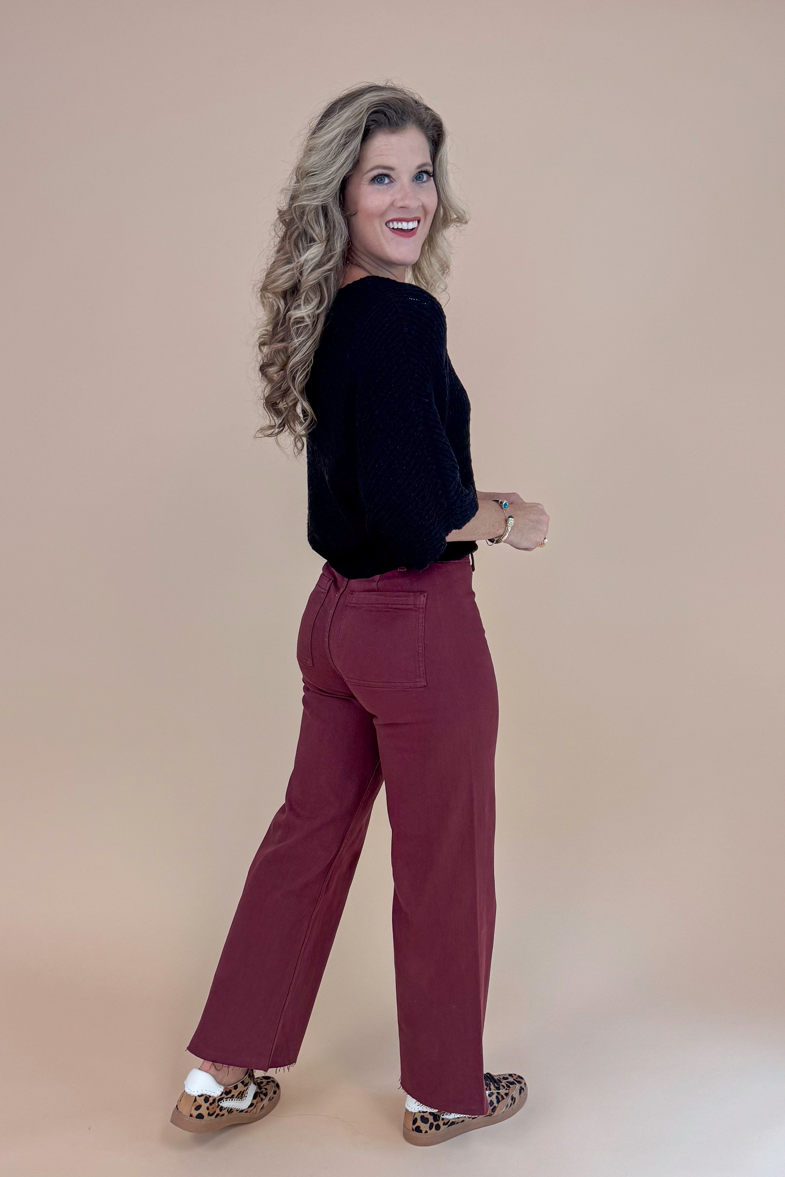 Woman wearing a black top and maroon pants against a beige background